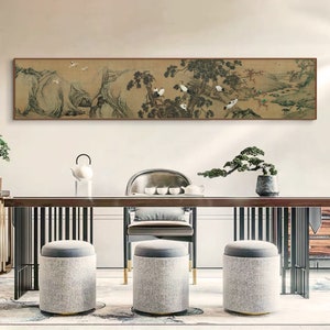 May include: A long, horizontal painting depicting a traditional Chinese landscape scene with mountains, trees, and birds. The painting is framed in a brown wood frame and hangs on a white wall above a wooden table with chairs and a teapot.