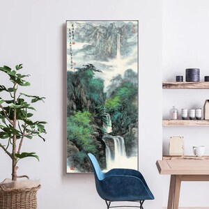 May include: A vertical painting of a waterfall cascading down a mountainside. The painting is done in a traditional Chinese style with brushstrokes and ink. The waterfall is surrounded by lush green trees and mountains. The painting is framed in a simple black frame.