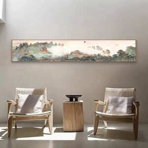 Pode incluir: Uma pintura longa e horizontal de uma paisagem montanhosa nebulosa com um sol vermelho no céu. A pintura está pendurada em uma parede branca acima de duas cadeiras de madeira com almofadas brancas.