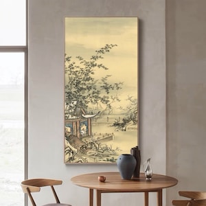 May include: A framed vertical artwork depicting a traditional Asian landscape. The painting features a pagoda, bridge, and trees along a body of water, with a muted color palette of beige, brown, and green. The artwork is displayed on a neutral-colored wall.