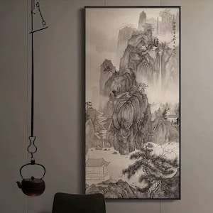 Pode incluir: Pintura a tinta da China monocromática de uma paisagem montanhosa com uma cachoeira, emoldurada em preto. Um serviço de chá com uma chaleira e xícaras brancas está sobre uma mesa. Uma chaleira suspensa e uma vela completam a cena.