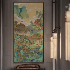 Könnte beinhalten: Gerahmtes Landschaftsgemälde, das eine traditionelle asiatische Szene darstellt. Das Kunstwerk zeigt Tempel, Brücken und Berge in Grün-, Blau- und Goldtönen. Das Gemälde wird an einer Wand mit dunkelgrauer Oberfläche ausgestellt.