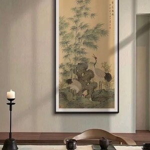 May include: Framed Asian-style artwork featuring a serene landscape with bamboo and three cranes. The painting has a muted color palette of greens, beige, and brown, with a black frame. The cranes are depicted in various poses, adding a sense of movement.