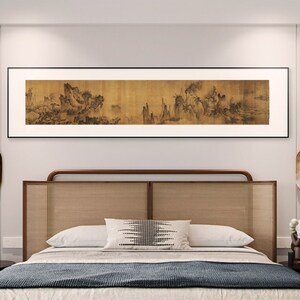 May include: A bedroom with a wooden bed frame with a woven headboard. The bed has a white and black patterned pillow and a dark blue blanket. A black and white painting of a landscape hangs above the bed.