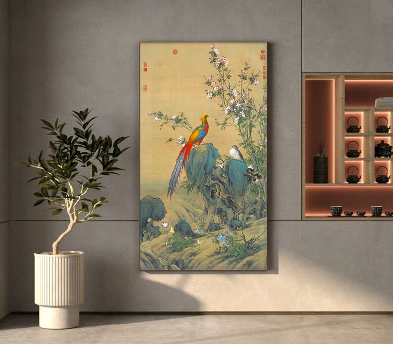 Op de afbeelding: Een vintage-stijl schilderij van een kleurrijke fazant die op een rots zit met een kleine vogel in de buurt. Het schilderij heeft een achtergrond van delicate roze bloemen en groene bladeren.