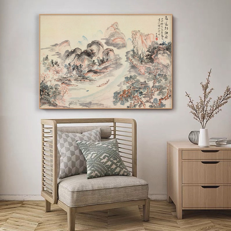 May include: A traditional Chinese landscape painting depicting mountains, trees, and a river. The painting is executed in shades of grey, blue, and pink, with a few touches of red. The painting is framed in a simple wooden frame.