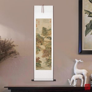 May include: A traditional Chinese scroll painting depicting a landscape scene with mountains, trees, and a river. The painting is done in shades of brown, green, and white, and is mounted on a white scroll with a brown wooden dowel at the top.