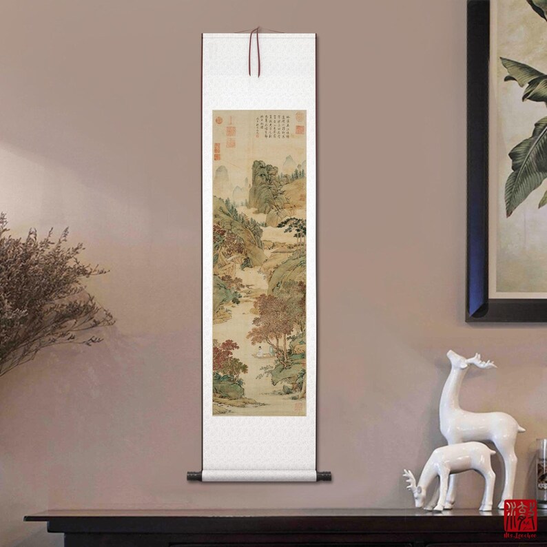 May include: A traditional Chinese scroll painting depicting a landscape scene with mountains, trees, and a river. The painting is done in shades of brown, green, and white, and is mounted on a white scroll with a brown wooden dowel at the top.
