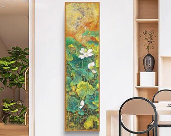 May include: Vertical framed painting featuring a white lotus flower and buds amidst green and yellow lily pads. The background has a textured, golden-orange hue. The artwork is displayed in a modern interior setting.