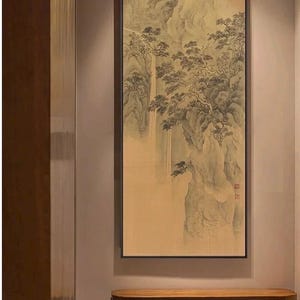 Könnte beinhalten: Gerahmtes Landschaftsgemälde mit schwarzem Rahmen. Das Kunstwerk zeigt eine Berglandschaft mit Wasserfällen und Bäumen in Beige-, Grau- und Schwarztönen. Das Gemälde wird über einer Holzbank ausgestellt.