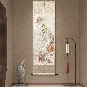 Op de afbeelding: Een traditioneel Chinees schilderij op een rol, dat een vrouwelijke godheid afbeeldt die omringd is door andere figuren in een bewolkte hemel. Het schilderij is gemonteerd op een houten frame en wordt aan een muur getoond.
