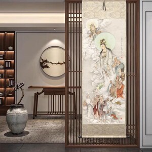 Op de afbeelding: Een traditioneel Chinees scroll-schilderij dat een vrouwelijke godheid afbeeldt die omringd is door figuren in een bewolkte hemel. Het schilderij is gemonteerd op een houten frame en klaar om opgehangen te worden.