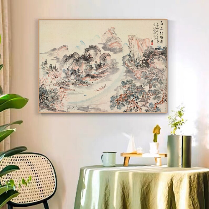 May include: A traditional Chinese ink and wash painting depicting a landscape scene with mountains, trees, and a river. The painting is done in shades of grey, black, and white, with hints of pink and blue. The painting is framed in a light wood frame.