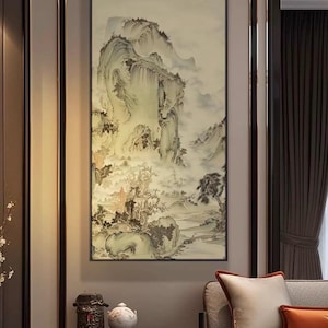 Könnte beinhalten: Gerahmtes Landschaftsgemälde, das eine neblige Berglandschaft in gedämpften Tönen von Beige, Grau und Grün zeigt. Das Kunstwerk weist einen traditionellen, asiatisch inspirierten Stil mit detaillierten Pinselstrichen und einer ruhigen Atmosphäre auf. Das Gemälde wird in einem Raum mit neutraler Farbpalette ausgestellt.