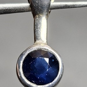 Puede incluir: Un colgante de plata con una piedra preciosa azul oscuro engastada en un bisel redondo.