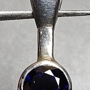Puede incluir: Un colgante de plata con una piedra preciosa redonda de color azul oscuro.