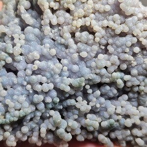 Puede incluir: Primer plano de un ágata de color púrpura claro y gris con una textura única y burbujeante. El ágata está cubierta de pequeños nódulos redondos que le dan un aspecto texturizado.