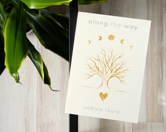 May include: A white card with gold lettering and illustrations. The card says "along the way" and features a tree with a heart at its base. The text "sabina laura" is at the bottom of the card.