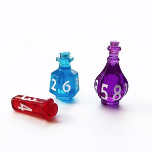 May include: Three glass dice in the shape of bottles. The dice are blue, purple, and red. The blue die has the numbers 2, 6, and 3 on it. The purple die has the numbers 5, 8, and 2 on it. The red die has the numbers 4, 3, and 2 on it.