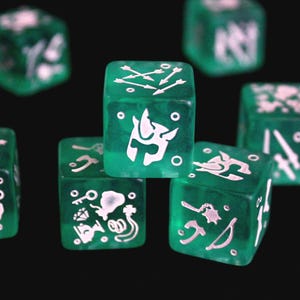 May include: A set of translucent green six-sided dice featuring white engraved icons. The visible faces display various symbols including a helmet, arrows, a key, a diamond, a pouch, a sword, a mace, and an axe, all arranged in a cluster.