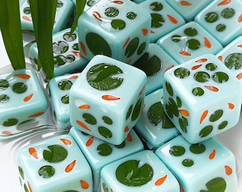May include: A collection of light blue dice featuring a pond-themed design with dark green lily pads and small orange koi fish patterns on each face. The dice have a smooth, glossy finish and are arranged in a cluster with green plant leaves.