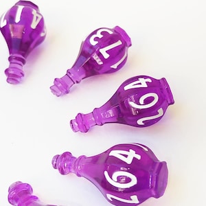 May include: Five translucent purple bottle-shaped beads, each featuring white printed numbers. The beads have a narrow neck and a rounded body, with visible numbers including 41, 173, 264, and 13. The objects are arranged in a scattered pattern.