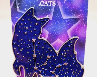 Puede incluir: Un pin de esmalte azul con dos gatos delineados en plata con una constelación de estrellas dentro de cada gato. El pin está sobre un fondo morado y azul con el texto "CONSTELLATION CATS" en la parte superior.