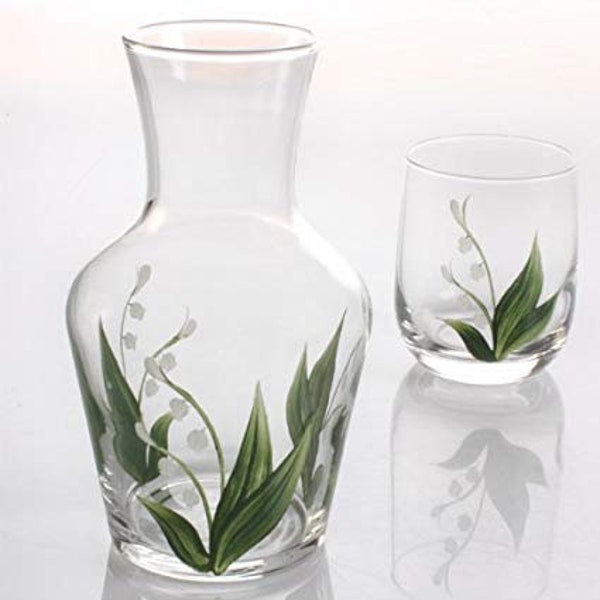 May include: A clear glass pitcher and tumbler with hand-painted lily of the valley designs. The pitcher has a wide base and a narrow neck. The tumbler is a standard size.