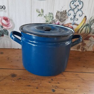 May include: A blue enamel pot with a lid and two handles. The pot is sitting on a wooden surface.