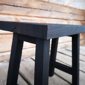 May include: A black wooden stool with a simple, rectangular design. The stool has a solid, sturdy construction and is perfect for adding a rustic touch to any space.