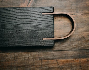 Puede incluir: Una bandeja de servir de madera negra con un asa de cuero marrón. La bandeja tiene un patrón de veta de madera natural y es perfecta para servir comida o bebidas.