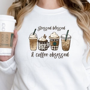 May include: White sweatshirt with the text "stressed blessed & coffee obsessed" and a graphic of four different coffee drinks.