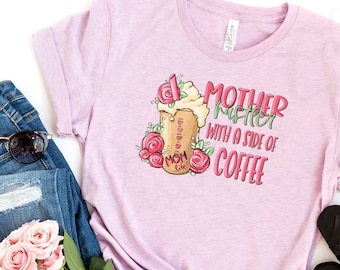 Puede incluir: Camiseta lila claro con el texto "MOTHER HUSTLER with a side of COFFEE" y un diseño de taza de café. La imagen incluye vaqueros azules, gafas de sol, bailarinas negras y un ramo de rosas rosas. Tema: ropa casual.