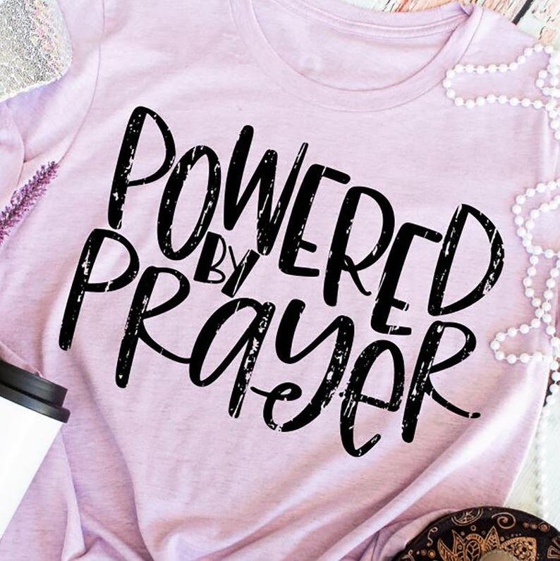 May include: A light purple t-shirt with the text "Powered by Prayer" in black distressed lettering.