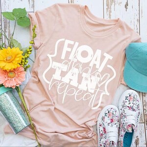 May include: A light pink t-shirt with the words "FLOAT, TAN, repeat" in white script, a turquoise baseball cap, and floral print shoes. A glittery tumbler and flowers are also in the image.