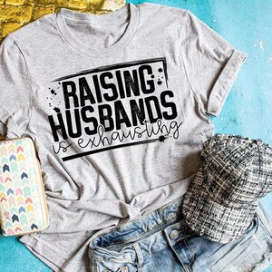 Peut inclure: Un t-shirt gris avec un texte noir qui dit "&Eacute;lever des maris est &eacute;puisant".