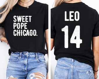 Könnte beinhalten: Schwarzes T-Shirt mit weißem Text "SWEET POPE CHICAGO." auf der Vorderseite. Auf der Rückseite des Shirts steht "LEO" über der Zahl "14" in Weiß. Das Shirt wird mit einer blauen Jeans getragen.