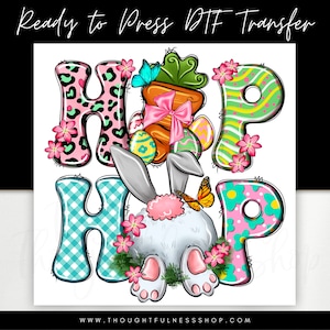 May include: A colorful Easter-themed graphic design featuring the words "Hop Hop" with a bunny rabbit in the center. The letters are decorated with polka dots, stripes, and animal print patterns. The bunny is white with pink ears and a pink tail.