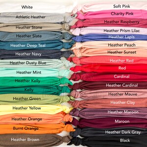 May include: A collection of folded t-shirts in various colors, including white, gray, pink, red, and black. Each shirt is labeled with its color name, such as "Heather Slate," "Heather Kelly," and "Maroon."