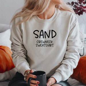 May include: A light beige crewneck sweatshirt with the text "SAND CREWNECK SWEATSHIRT" in black.