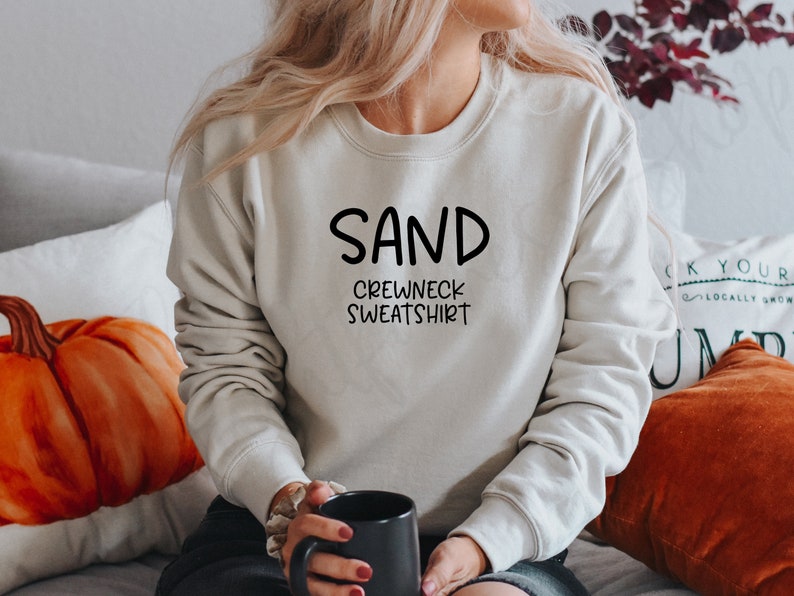 May include: A light beige crewneck sweatshirt with the text "SAND CREWNECK SWEATSHIRT" in black.