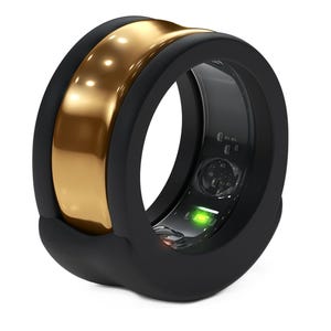 May include: A black smart ring with a gold band. The ring has a sleek, modern design with a glossy gold center and a matte black exterior. A small green light is visible inside the ring.