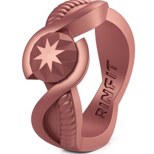 Op de afbeelding: Een ros&eacute;gouden siliconen ring met een stervormig ontwerp en het woord "RINFIT" gegraveerd aan de zijkant.