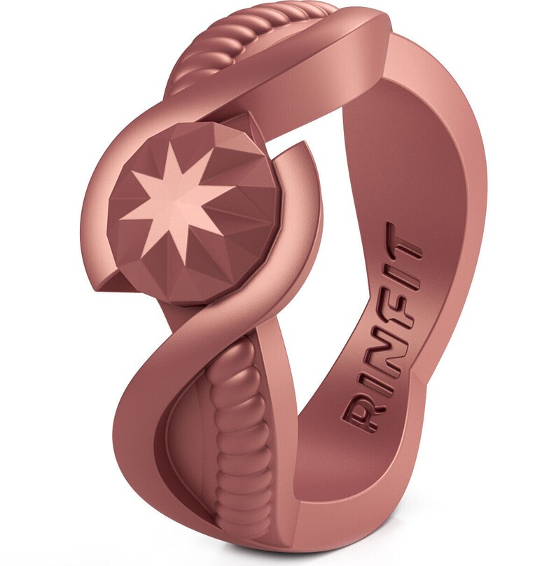 Op de afbeelding: Een ros&eacute;gouden siliconen ring met een stervormig ontwerp en het woord "RINFIT" gegraveerd aan de zijkant.