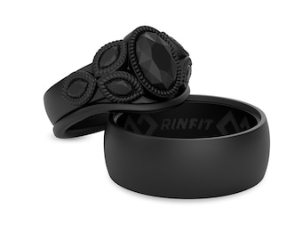 Op de afbeelding: Twee zwarte ringen, een met een zwarte edelsteen en ingewikkelde details, en de andere een eenvoudige siliconen band met het woord "RINFIT" erop gegraveerd.