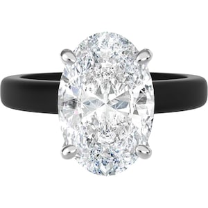 May include: A ring featuring a large, clear, oval-cut gemstone held by four silver-toned prongs. The band of the ring is a solid, matte black color with a smooth, rounded surface, creating a high-contrast look between the stone and the band.