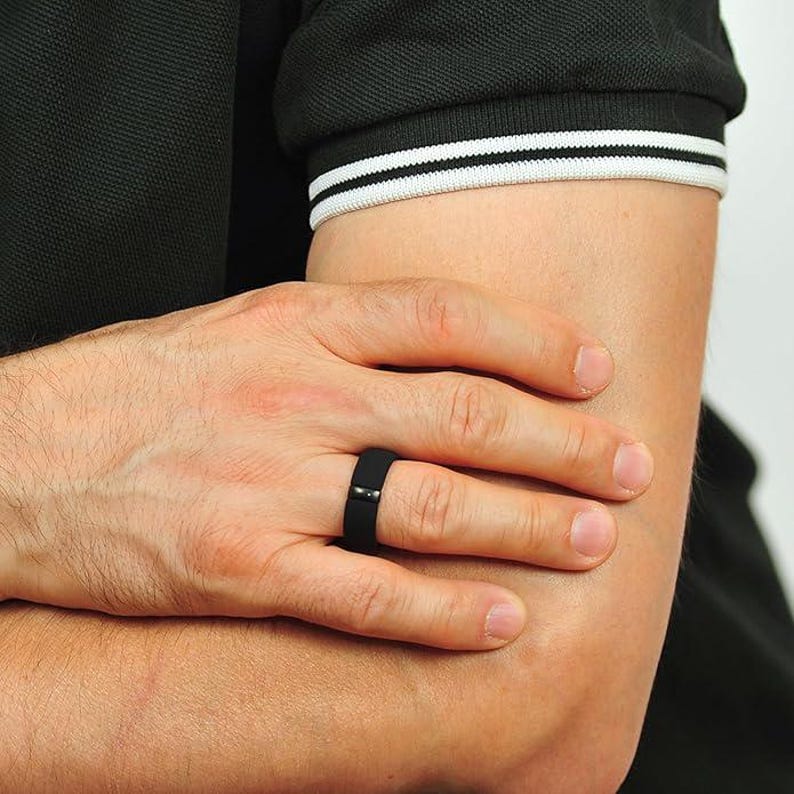 May include: A black silicone ring with a black inlay. The ring is worn on the ring finger of a person's left hand.