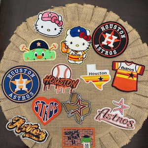 May include: A collection of embroidered patches featuring Houston Astros baseball themes, including Hello Kitty characters, team logos, a baseball, the state of Texas, a jersey, a heart shape, and a brick wall graphic with the text Bury Me In The H.