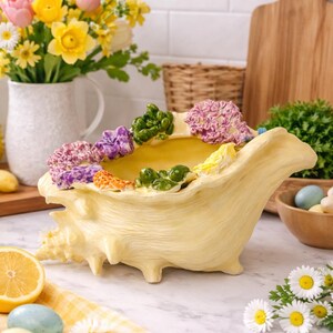 May include: A handmade wooden sign with the text "Welcome" in a whimsical font. The sign is painted white with a distressed finish, and features a decorative floral design in shades of pink and green. It is designed to be hung on a wall.