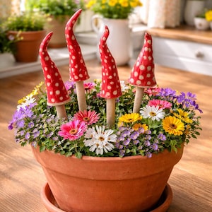 May include: A terracotta flower pot filled with colorful flowers and decorative mushroom stakes. The mushrooms have red caps with white polka dots. The flowers include pink, white, yellow, and purple blooms.